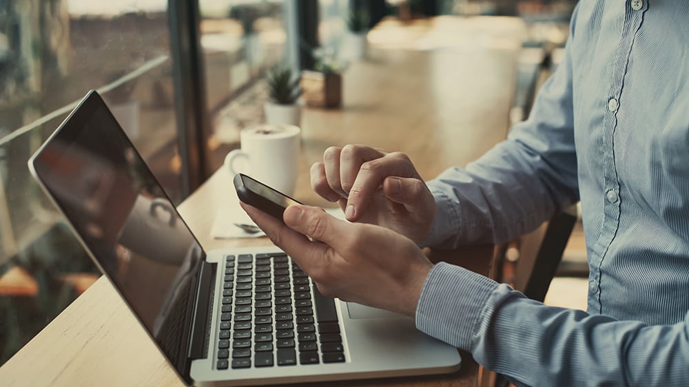 Close up of person using a laptop and their phone